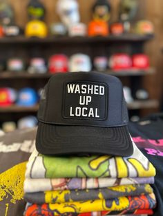 a black hat that says washed up local on top of several shirts in a store