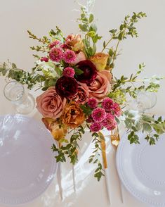 an arrangement of flowers on a table with plates and utensils in the foreground