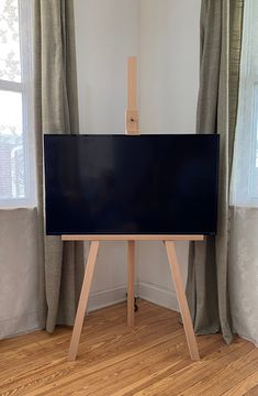 an easel stands in front of a flat screen tv on a wooden stand next to two windows