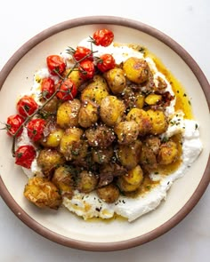 a white plate topped with potatoes covered in sauce and garnished with cherry tomatoes