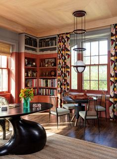 the dining room is decorated in red and black with bookshelves, windows, and chairs