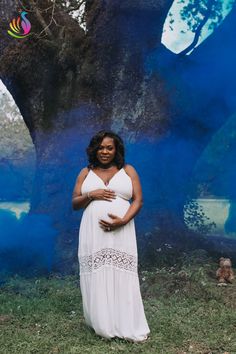 a pregnant woman standing in front of a blue tree with her belly wrapped around her waist