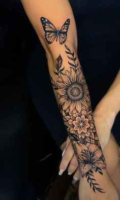 two women with tattoos on their arms holding each other's hands, one has a butterfly and the other has sunflowers