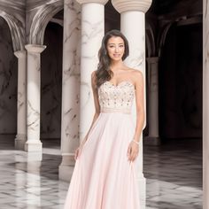 a beautiful woman in a pink dress posing for a photo with columns and pillars behind her