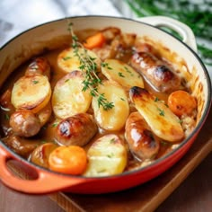 a red pot filled with potatoes and sausages on top of a wooden cutting board