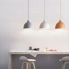 three pendant lights hang over a table with two stools in front of it,