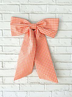 an orange and white gingham bow hanging on a brick wall