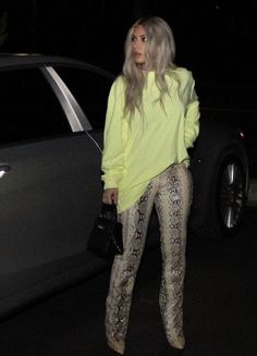 a woman standing next to a car wearing snakeskin leggings and a yellow sweater