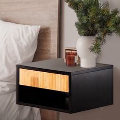 a night stand with a plant on top of it next to a white vase and bed