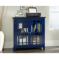 a blue cabinet with glass doors and bookshelf in the corner next to a window