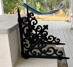 a black iron clock sitting on the side of a porch next to a hammock