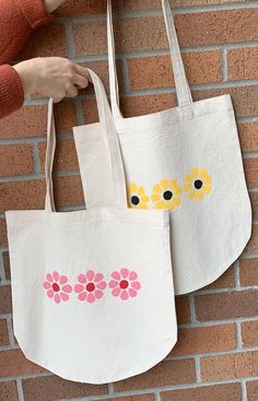 two white bags with yellow and pink flowers painted on them hanging from a brick wall