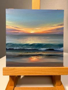 an easel with a painting on it that has a sunset over the ocean and waves