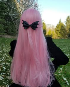 a woman with long pink hair wearing a black bow on it's head, sitting in the grass