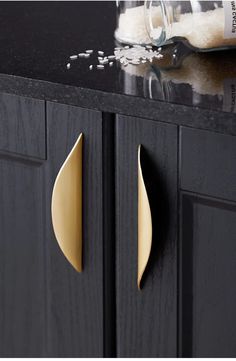 a black cabinet with two gold handles and some grains on the counter top next to it