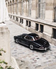 an old black car parked in front of a tall building on a cobblestone street