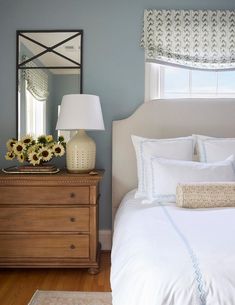 Bedroom with blue walls features a cream pierced lamp that illuminates a French dresser as nightstand under a mirror and a crisp white headboard with white and blue bedding.