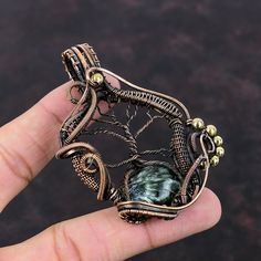 a hand holding a wire wrapped brooch with a green bead around it's center