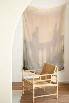 a chair sitting on top of a hard wood floor next to a window covered with a sheer curtain