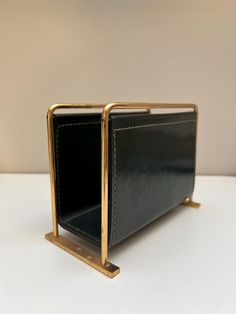 a black and gold leather purse on a white table with a metal holder in the shape of a rectangle