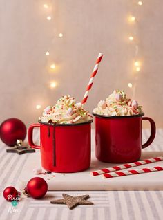 two red mugs filled with whipped cream and candy cane on top of a table