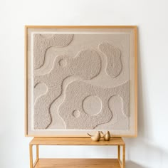 an art piece is displayed on a shelf in front of a white wall and wooden table