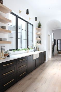 a kitchen with black cabinets and white counter tops, wooden flooring and open shelving