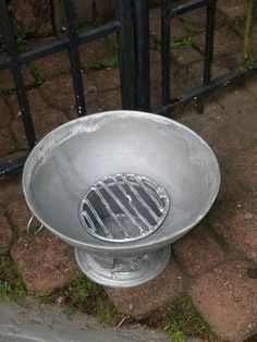 a metal bowl sitting on the ground next to a fence