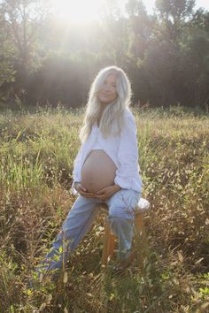 a pregnant woman sitting on a stool in a field