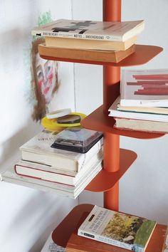 three tiered bookshelf with magazines stacked on each other in front of a white wall