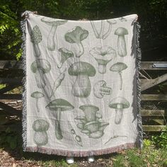 a green and white blanket with mushrooms on it hanging from a wooden fence in the grass