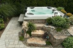 an outdoor hot tub surrounded by rocks and plants