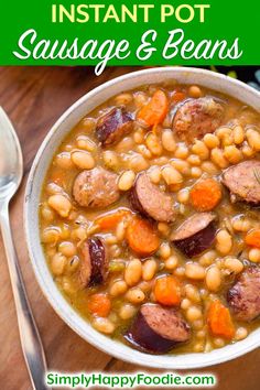 a white bowl filled with sausage and beans next to a spoon on top of a wooden table