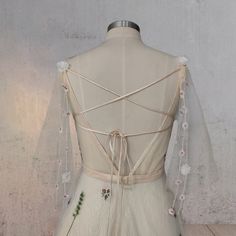 the back of a wedding dress with flowers and ribbons on it, sitting on a mannequin