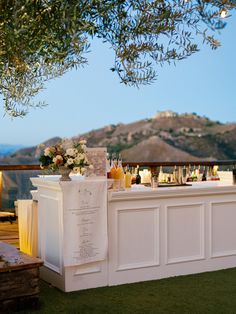 an outdoor bar is set up with bottles and glasses on the counter, along with flowers