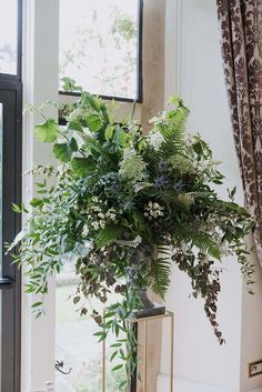 a vase filled with lots of greenery next to a window