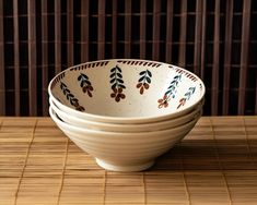 four white bowls sitting on top of a wooden table next to a bamboo mat covered wall