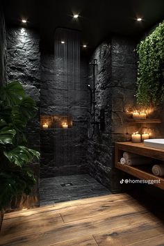 a bathroom with black stone walls and wood flooring is lit by candles in the shower