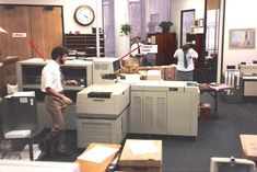 two men are in an office setting with boxes and computers on the desks,