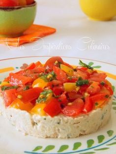 a plate topped with a cheesecake covered in tomatoes and green herbs next to a bowl of lemons