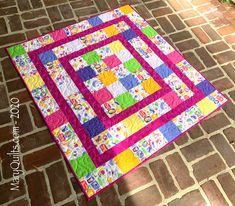 a pink and green patchwork quilt sitting on top of a brick floor