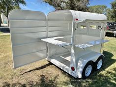 a white trailer is parked in the grass with its door open and shelves on it