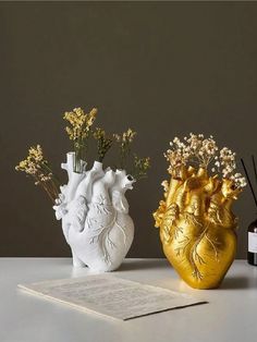 two vases with flowers in them sitting on a table next to an open book