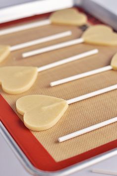 several pieces of heart shaped cookies on a cookie sheet with white sticks sticking out of them