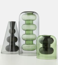 three glass vases sitting next to each other on a white counter top, one is green and the other is black