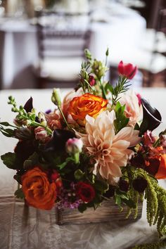 a wooden box filled with lots of flowers on top of a white cloth covered table