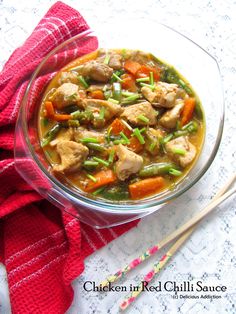 a glass bowl filled with chicken and veggies next to chopsticks on a table