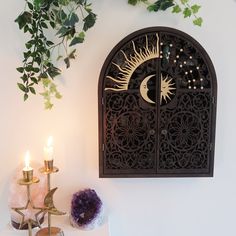 a wall mounted clock on the side of a white wall next to candles and plants