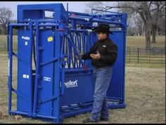 a man standing next to a blue box in the middle of a grass covered field