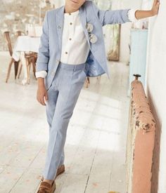 a young boy in a blue suit leaning against a wall with his hand on the door handle